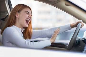 Closeup portrait of pissed off displeased angry aggressive woman driving a car shouting at someone with hand fist up. Negative human expression consept.