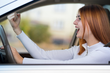 Closeup portrait of pissed off displeased angry aggressive woman driving a car shouting at someone with hand fist up. Negative human expression consept.