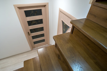 Interior of a house or appartment hallway with oak wooden stairs and room doors.