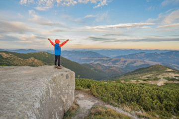Obraz premium Young child boy hiker standing with raised hands in mountains enjoying view of amazing mountain landscape at sunset.