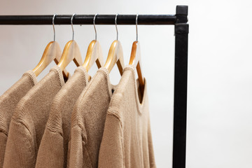 Warm woolen sweaters beige color hanging on hangers