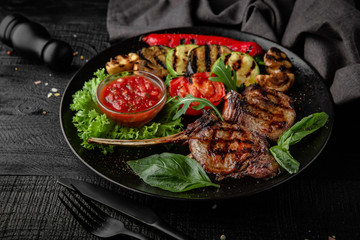 Rack of lamb calf with grilled vegetables, herbs and spicy tomato sauce. Nutritious, dietary, fitness food. Black boards background