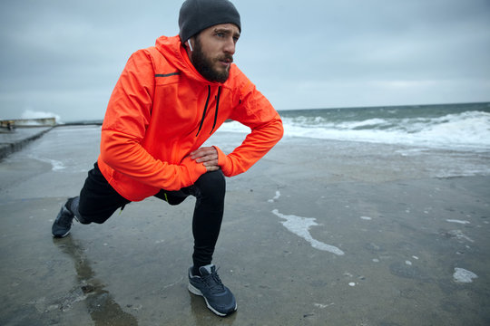 Portrait of active attractive young bearded man stretching muscules and doing warm-up before morning run, starting day from morning jog. Fitness and sport concept