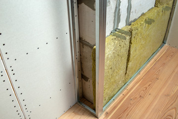 Wall of a room under renovation with mineral rock wool insulation and metal frame prepared for drywall plates.