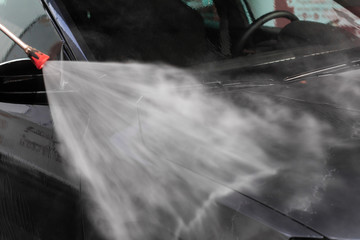 A man is washing a car at self service car wash. High pressure vehicle washer machine clean with...
