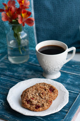 Oatmeal cookies, black coffee and a bouquet of red flowers stand on a tray in bed.