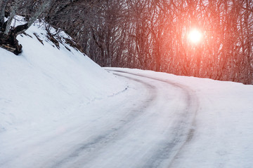 first snow on the road in forest at sunset