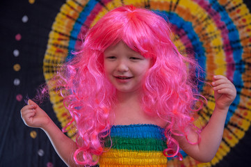 Happy Cute caucasian boy changed clothes at carnival in dress of girl of rainbow color. Pink doll wig. LGBT color background. Education in kindergarten and preschool children. hair coloring
