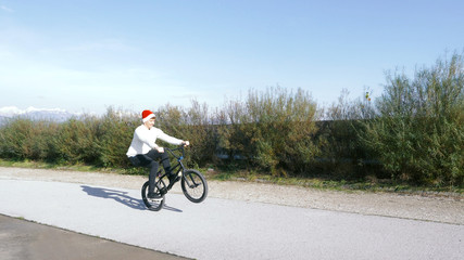 Extreme bmx biker riding manual trick in sunny park with santa claus hat