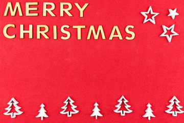 The Inscription Merry Christmas made of wooden letters, lying flat from above, isolated on a red, rough background. White wooden Christmas trees arranged in a row at the bottom.
