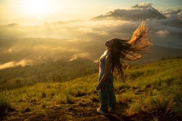 Beautiful girl with long hair on the volcano Batur on the island of Bali. Indonesia at sunrise. A lot of sun