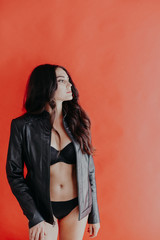 brunette girl in leather jacket and black lingerie on a red background