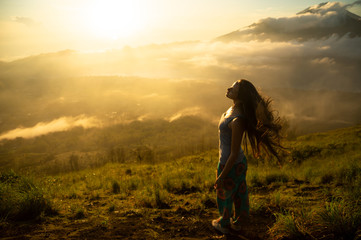 Fototapeta premium Beautiful girl with long hair on the volcano Batur on the island of Bali. Indonesia at sunrise. A lot of sun
