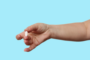 female hand holds out, offering, white elongated pill, close-up, color background, copy space, concept of medical care, treatment