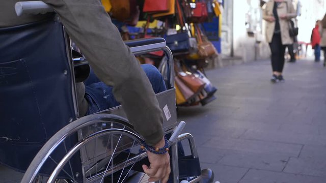 disabled man in his wheelchair passing in front of a bag's stall in the street