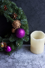 Artificial candle and half of a Christmas wreath decorated with bright pink Christmas balls, anise, nuts, cones on a gray background