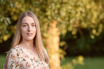 Fototapeta premium Portrait of a young blonde woman against a defocused landscape. Autumn color shade.