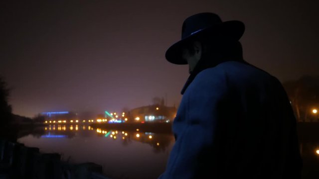 lonely man with hat and coat walking at night city with river