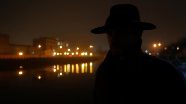 silhouette of man with hat in night city with river