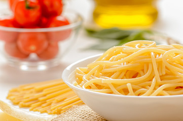 Durum wheat pasta on a white background with a decanter of olive oil, basil and a tomato