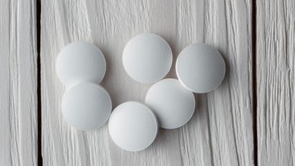 white pills on white wooden background close up