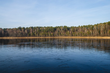 Winter landscape of the lake which is not frozen . The shore of the lake at sunset.