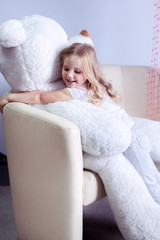 girl sitting on a big white teddy bear and playing with pink beads