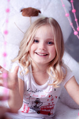 girl sitting on a big white teddy bear and playing with pink beads