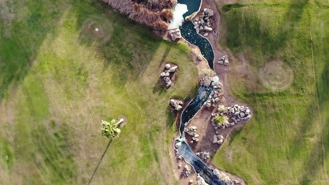 Aerial view of golf course. Cinematic top view 4K footage with green grass, ponds, watercourses, palm trees, patches, holes, flags. Evening time shot during sunset, soft golden light 