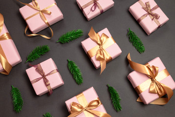 Obraz na płótnie Canvas Holiday pattern of assorted gifts wrapped in a pink thought with a gold awning and green sprigs of fir on a dark background. Top view with copy space. Flat lay creative idea design