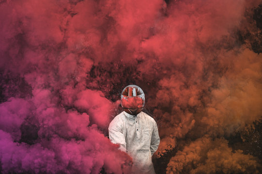 guy in mask standing in between pink, purple and orange smoke bombs