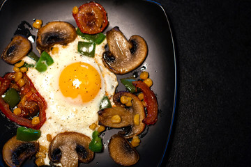 Freshly fried scrambled eggs with vegetables on a black plate