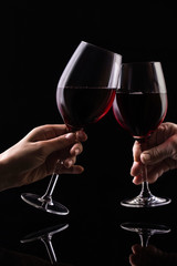 Two glasses with red wine in the hands of people on a black background. Wine on the dark