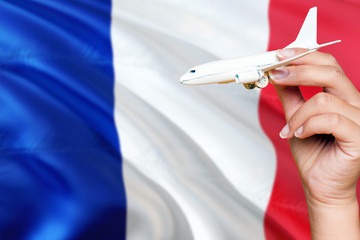 France travel concept. Woman holding a miniature plane on national flag background. Holiday and voyage theme with copy space for text.