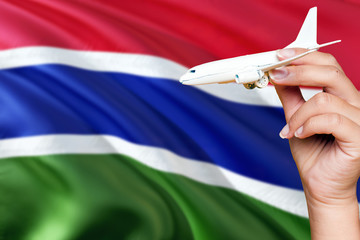 Gambia travel concept. Woman holding a miniature plane on national flag background. Holiday and voyage theme with copy space for text.
