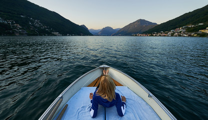 Una mujer tumbada en una barca disfrutando de las vistas al lago y montañas.