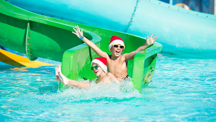 Children in Santa Claus hats ride on a water slide.New Year, Christmas.	