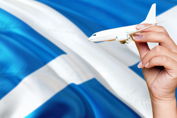 Scotland travel concept. Woman holding a miniature plane on national flag background. Holiday and voyage theme with copy space for text.