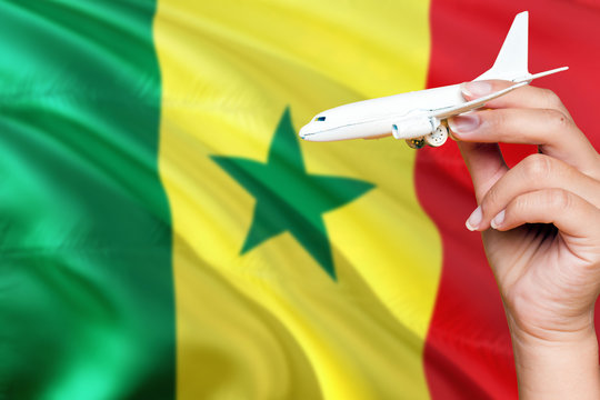 Senegal travel concept. Woman holding a miniature plane on national flag background. Holiday and voyage theme with copy space for text.