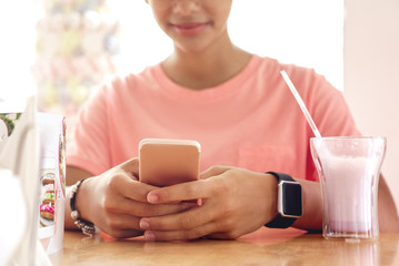 In the Cafe. Young girl sitting at table with milkshake playing smartphone joyful close-up