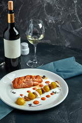 A large roasted piece of red fish lies on a white plate with vegetables, a beautiful serve in a restaurant