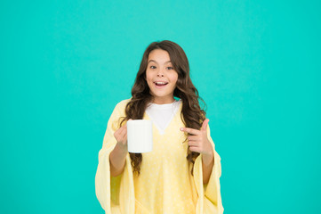 Starting day with breakfast. small kid turquoise background. little girl drink cocoa or milk before sleeping. cosy and fluffy pajama. feeling comfortable at home. happy girl with hot dring in cup