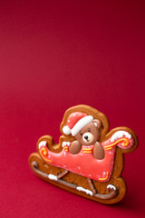gingerbread cookie of teddy bear on sleigh on red background. Traditional Christmas food. Christmas and New Year holiday concept. Copyspace