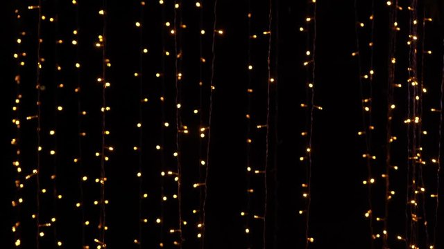 Many glowing golden lights of led holiday garlands shining in darkness of night. Abstract festive background. Real time 4k video footage.