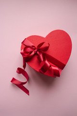 Red gift box heart shape with red ribbon on a pink background, gift concept