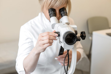 Female blond doctor gynecologist looks through a colposcope. Examination by a gynecologist. Female health concept