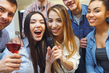 Group of friends having party indoors fun singing karaoke together close-up