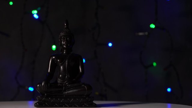 Black Buddha statue on a black grange background with a blinking garland