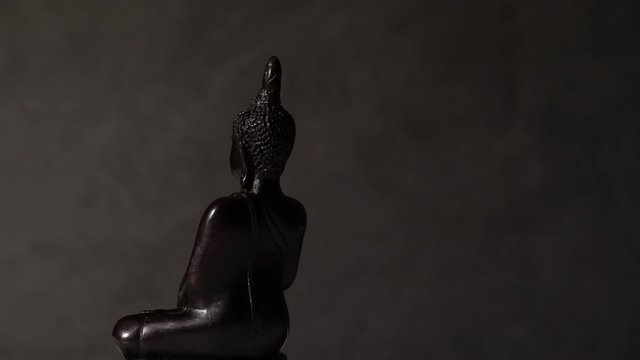 Black Buddha figurine rotates on a black grange background