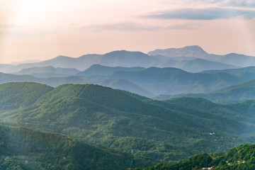Fototapeta premium Layers of mountains in the haze during sunset. Beautiful sunset in the hills and mountains. Beautiful sunset in a hilly valley with fog in the lowlands.
